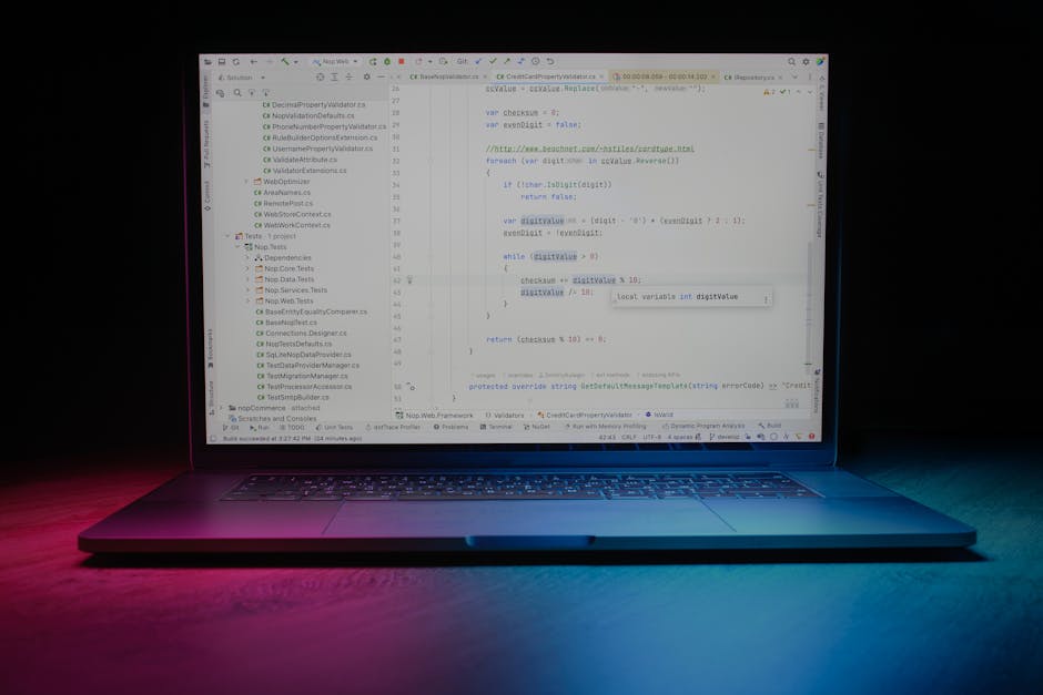 A modern laptop computer with a black keyboard and a large screen displaying lines of programming code, primarily in shades of blue, white, and green. The laptop is positioned on a dark surface and is